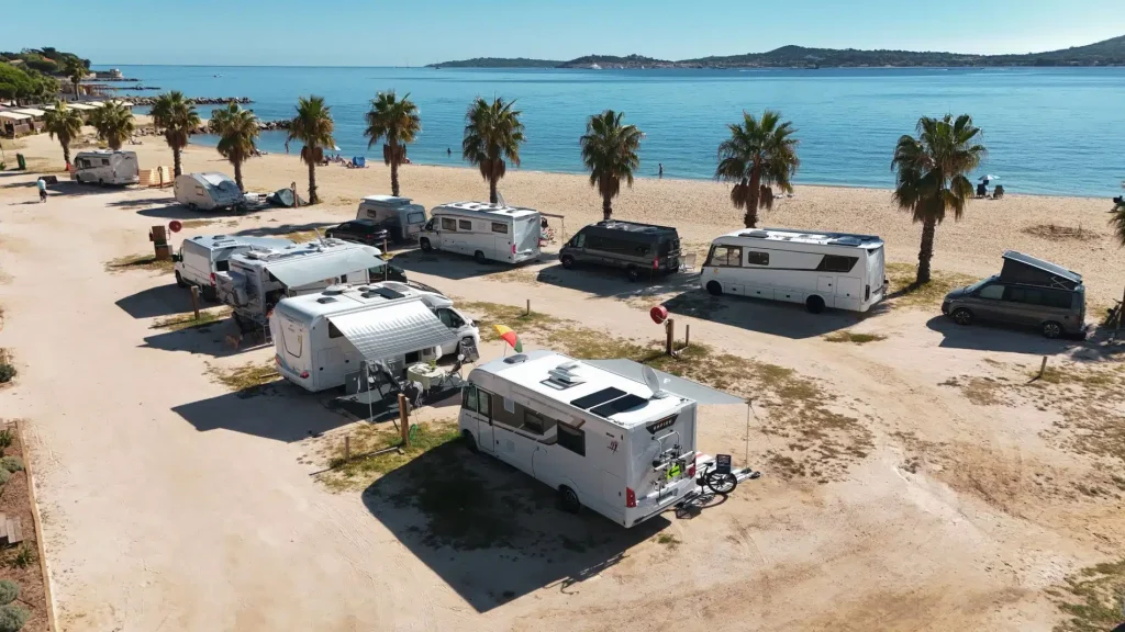 Wohnmobile und Wohnwägen stehen in einer ruhigen Bucht direkt am Stand des Mittelmeeres - Sinnbild für außergewöhnliche Campingplätze in Europa.