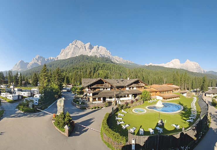 Panorama des Caravanpark Sexten mit Stellplätzen, Hauptgebäude und den beeindruckenden Sextner Dolomiten in Südtirol.